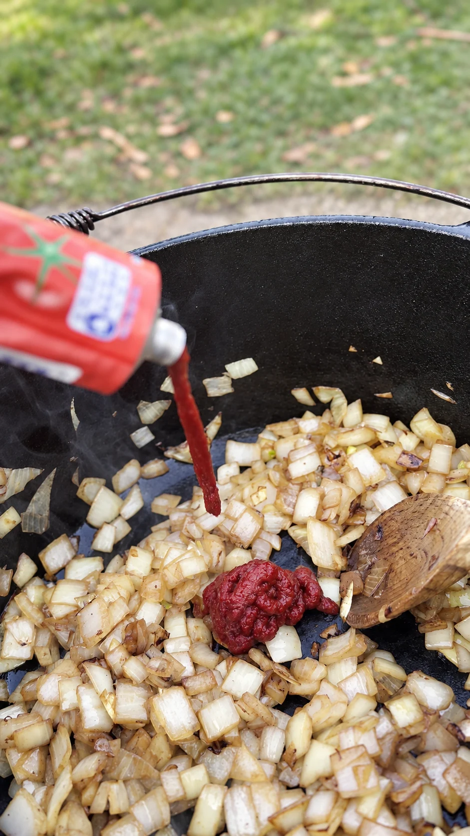 Tomatenmark wird zu angebratenen Zwiebeln im Dutch Oven gegeben.