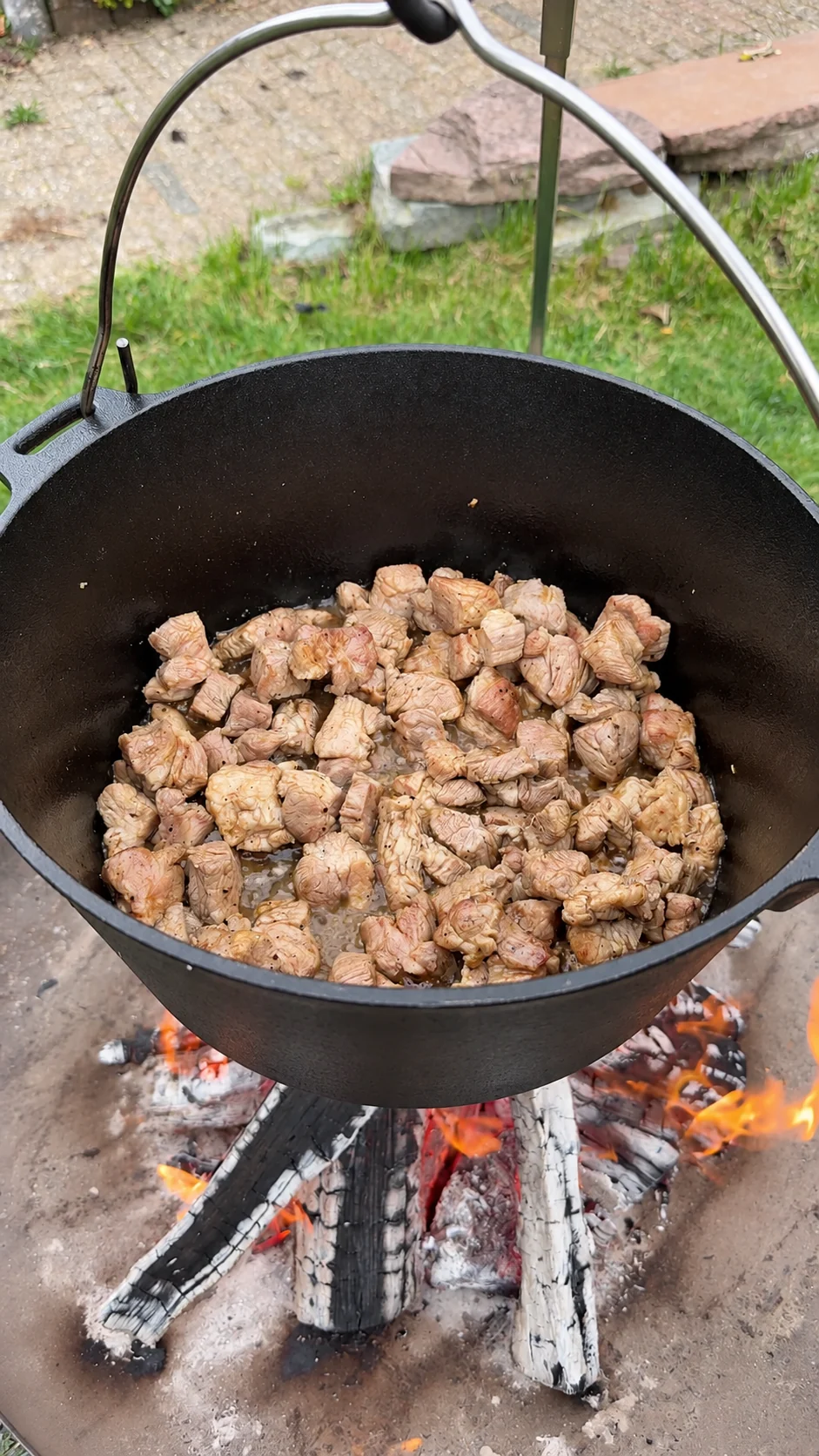 Schweinegulasch wird im gusseisernen Topf über offenem Feuer angebraten.