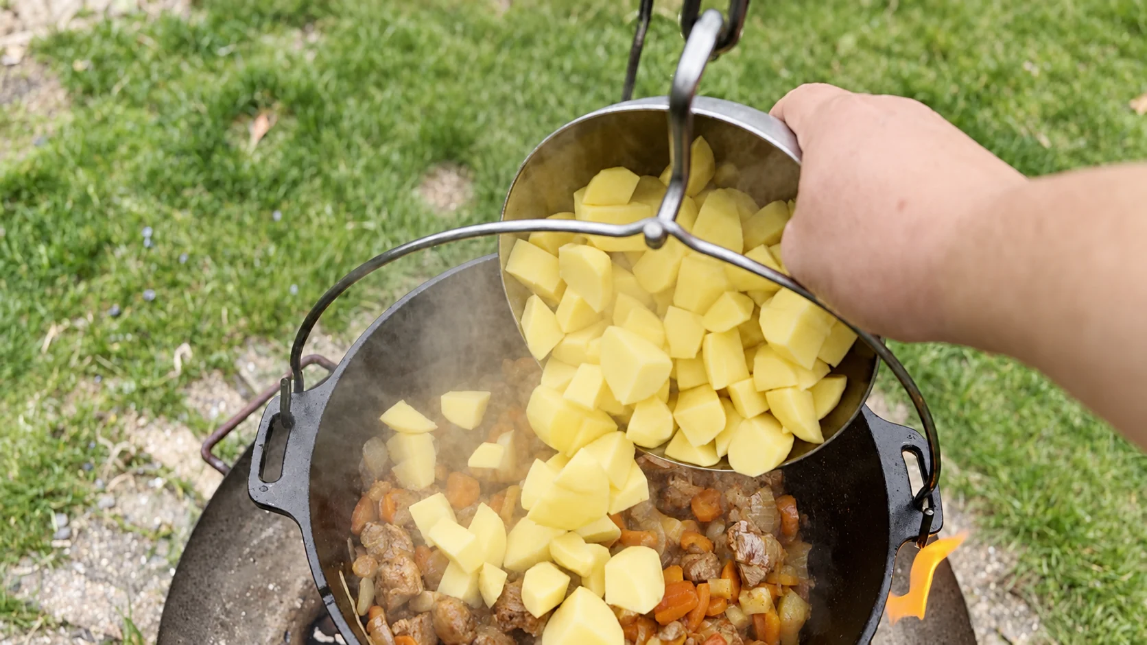 Geschälte Kartoffelwürfel werden aus einer Metallschüssel in den Feuertopf gegeben.