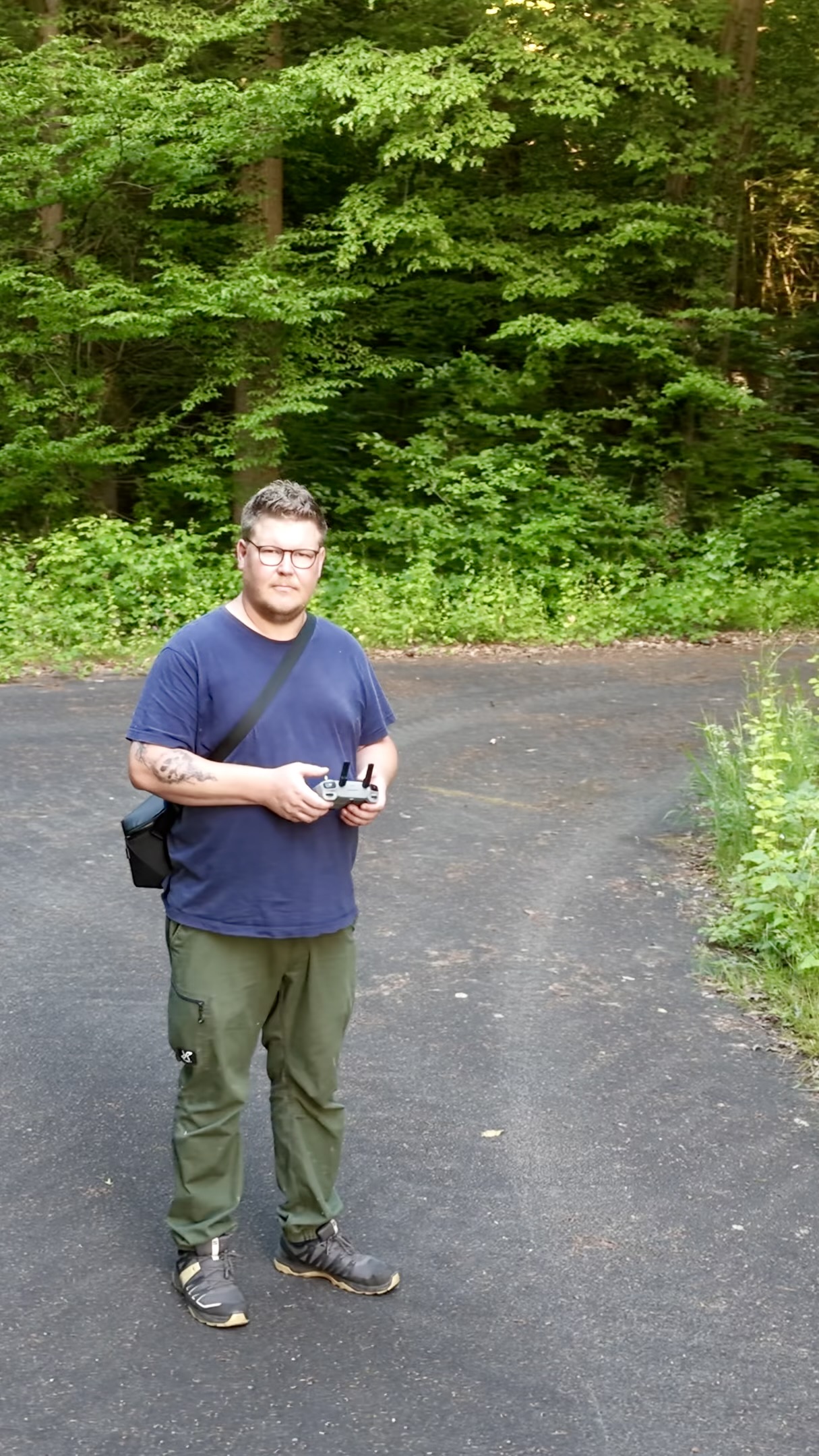 Florian steht mit einer Fernsteuerung auf einem Weg im Wald