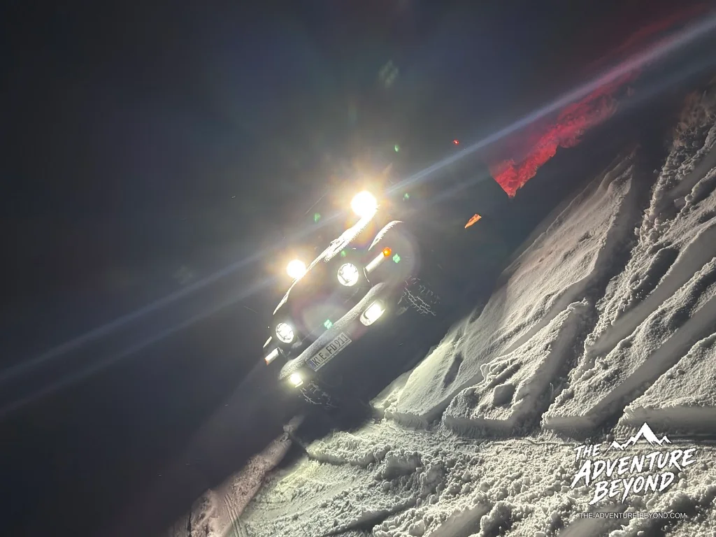 Jeep mit eingeschalteten Scheinwerfern bei der nächtlichen Wintertour durch den verschneiten Reichswald