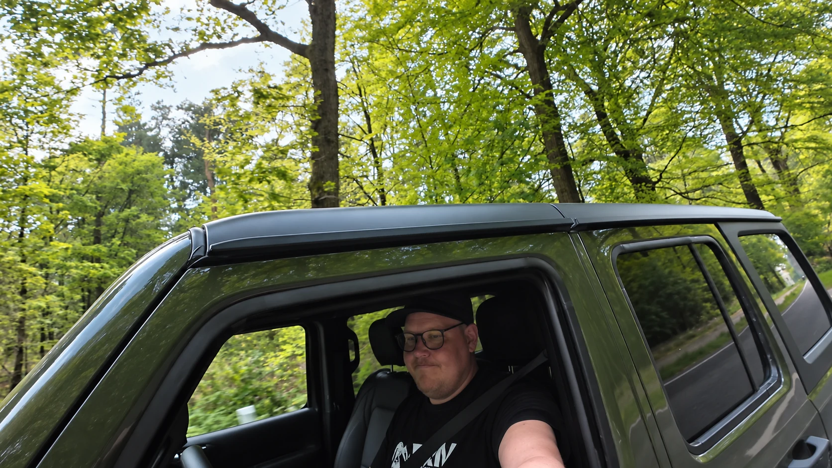Florian im olivgrünen Jeep vor grünen Bäumen, bevor der starke Regen einsetzt