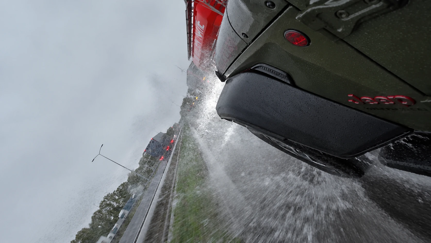 Seitliche Bordkameraperspektive am Jeep mit einer kräftigen Spritzwasserfahne auf der Straße