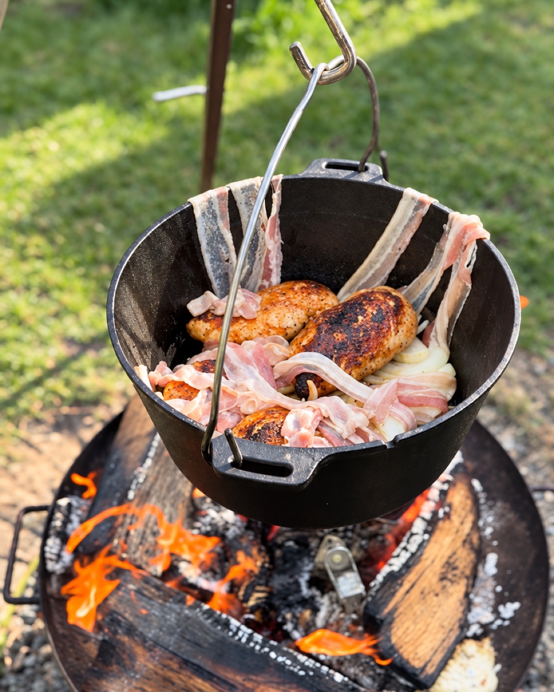 Ein Dutch Oven mit Hähnchen, Bacon und Zwiebeln hängt über dem Feuer.