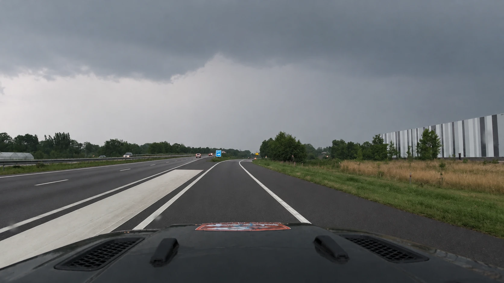 Graue Gewitterwolken und aufgehellter Horizont über der Autobahn vor der Jeep-Motorhaube