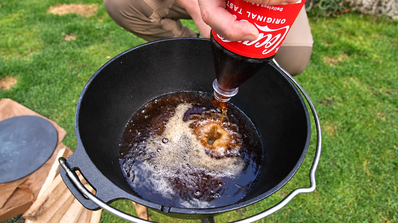 Cola wird aus einer Flasche in den schwarzen Dutch Oven gegossen.