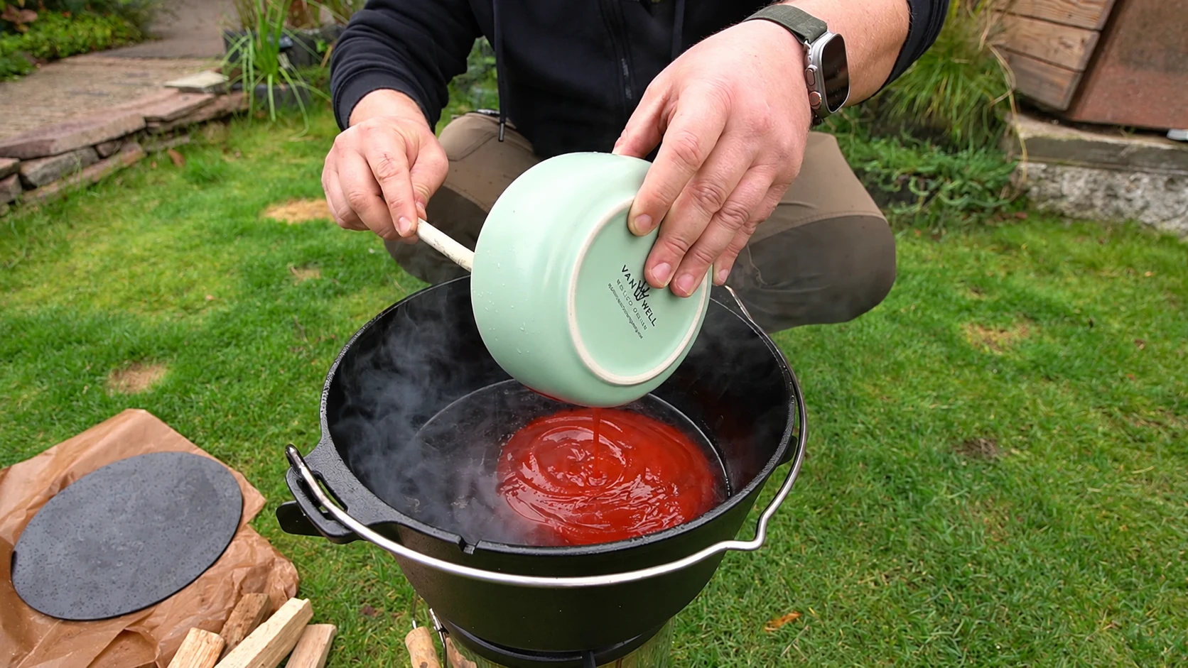 Eine grüne Schüssel wird über dem Dutch Oven ausgekratzt; Tomatenketchup fließt in den Topf.