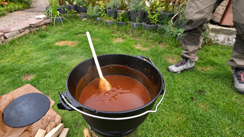 Rotbraune Currysauce mit Holzlöffel in einem schwarzen Dutch Oven im Garten.