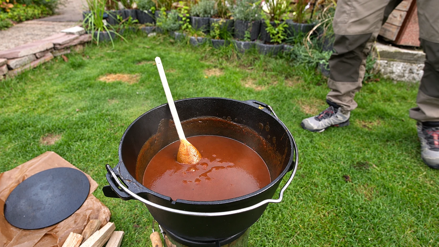Rotbraune Currysauce mit Holzlöffel in einem schwarzen Dutch Oven im Garten.