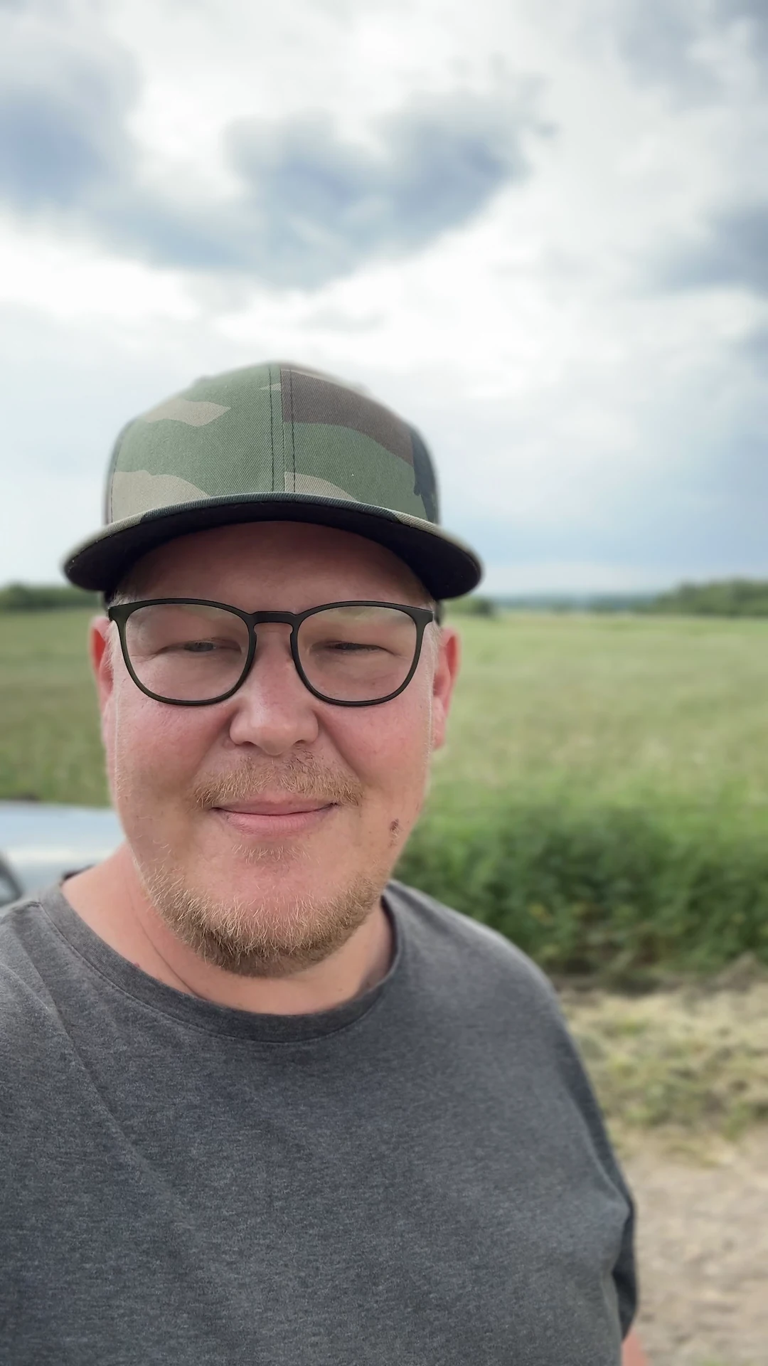 Florian mit Cap und Brille am Feldrand vor einem bewölkten Himmel.