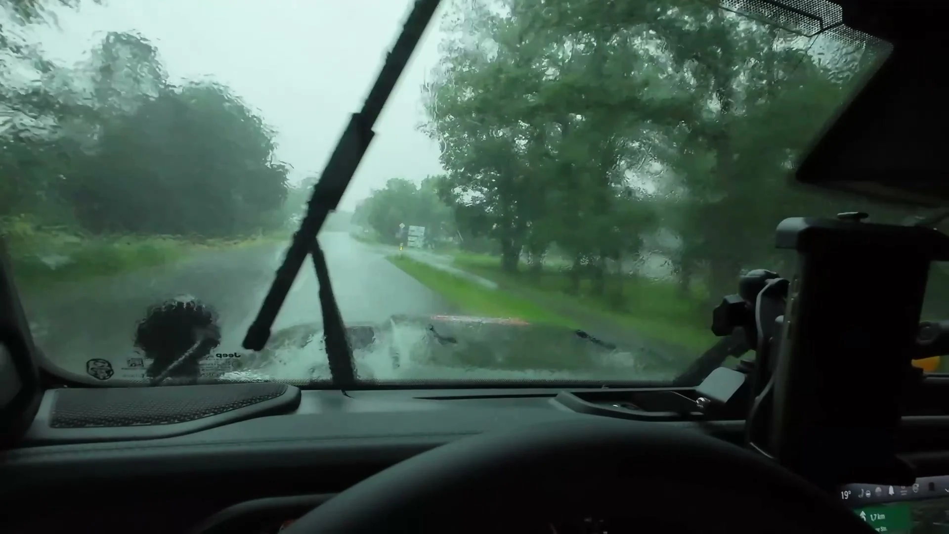 Regenwasser auf der Windschutzscheibe des Jeeps, ein Scheibenwischer und eine nasse Straße.