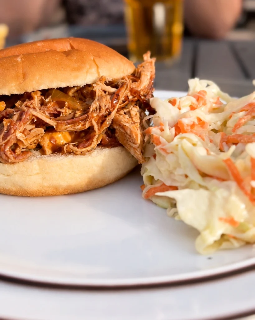 Pulled-Chicken-Burger mit BBQ-Sauce und cremigem Coleslaw auf einem weißen Teller.