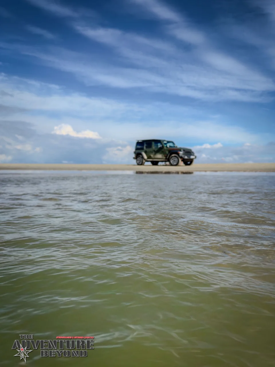 Der Jeep am weiten Strand, davor ein flacher Wasserlauf.
